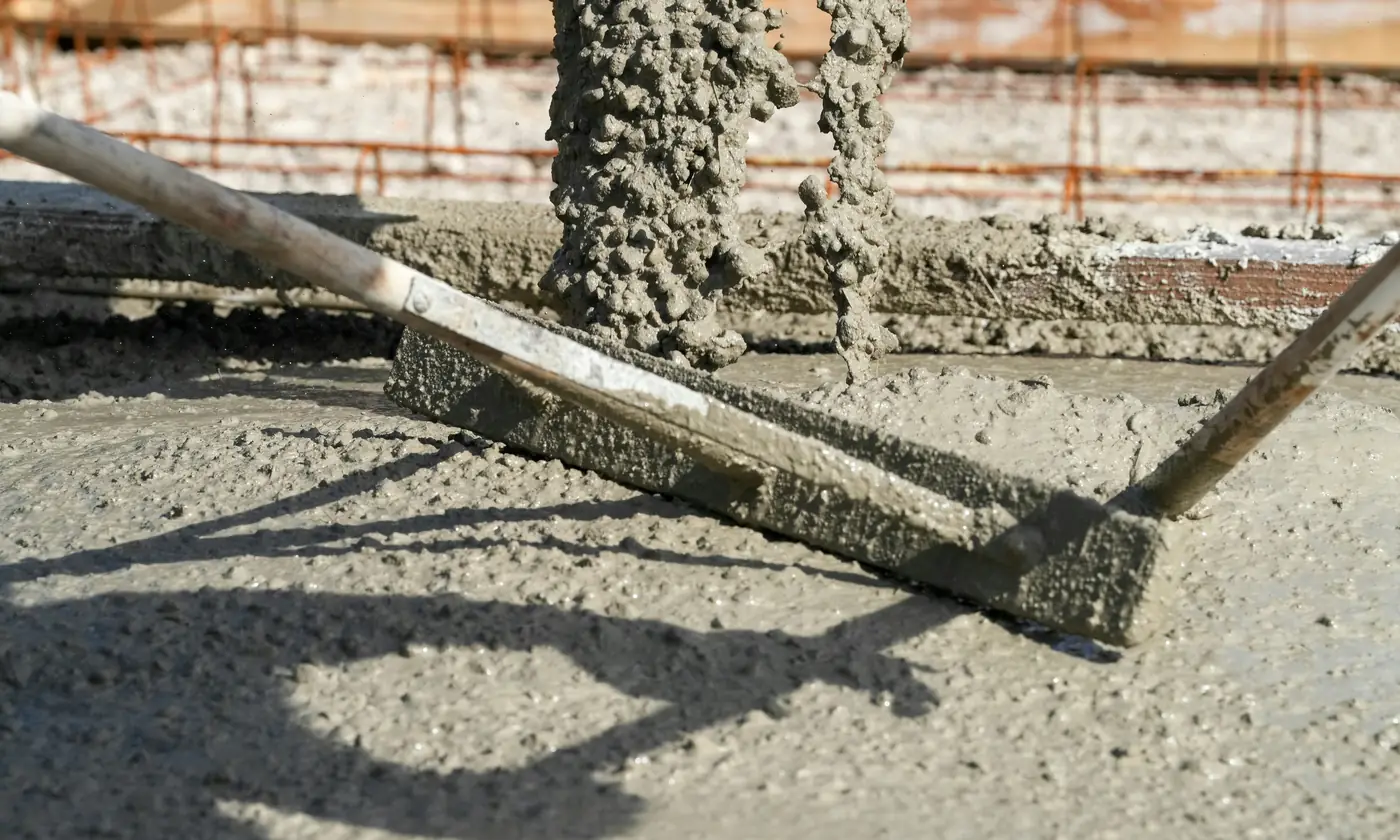 Wet concrete being spread over steel reinforcing for a new slab